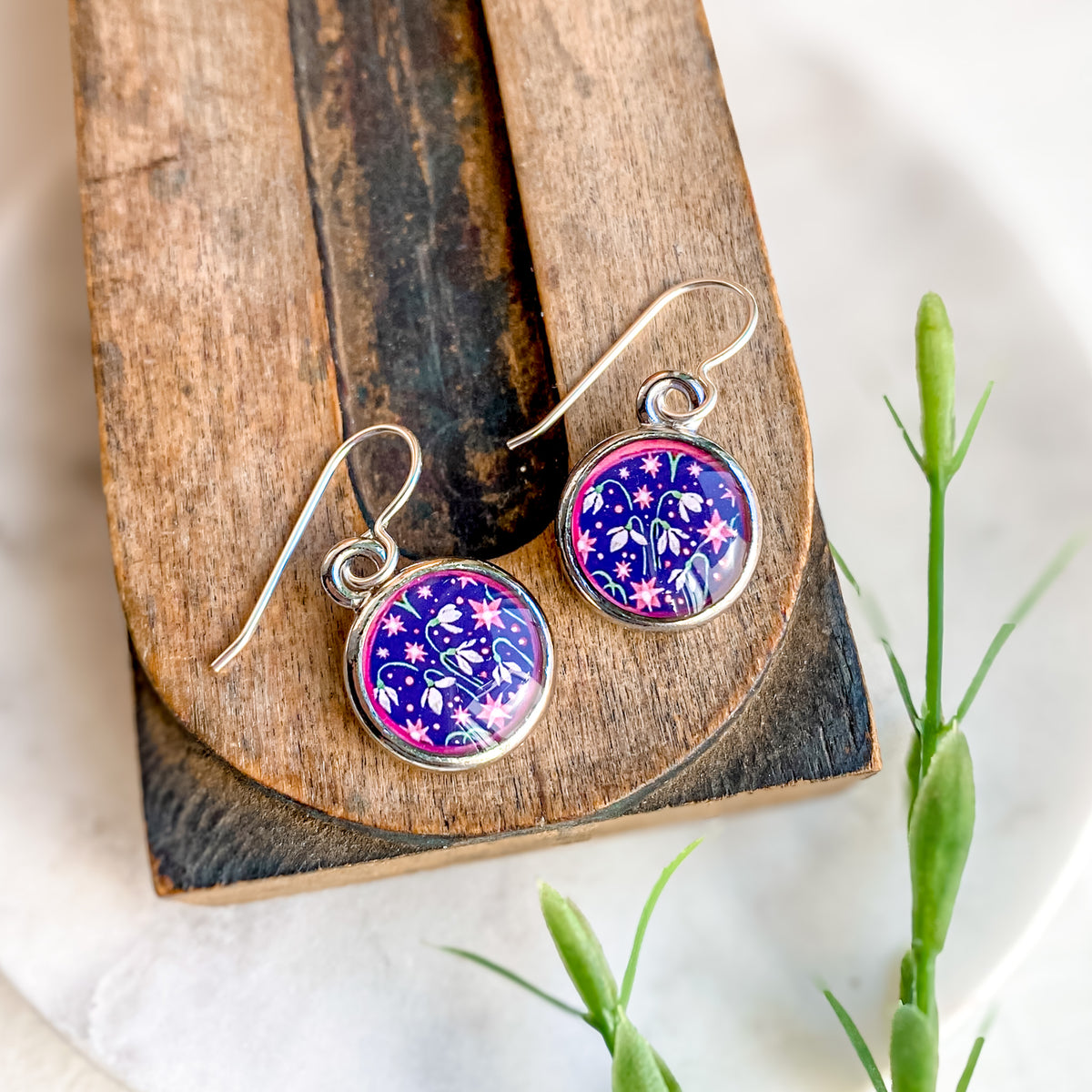 a pair of earrings sitting on top of a piece of wood