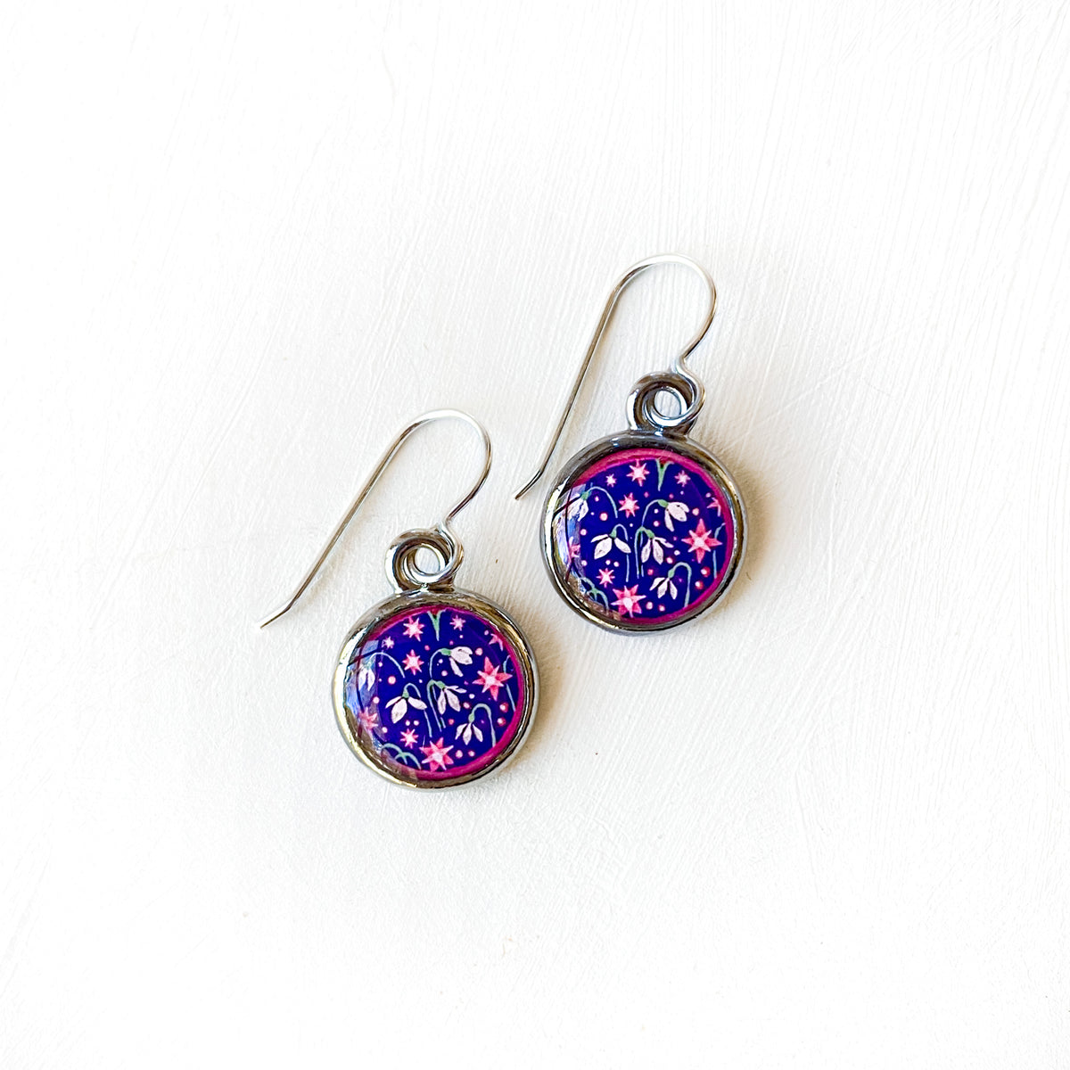 a pair of purple and pink earrings on a white surface