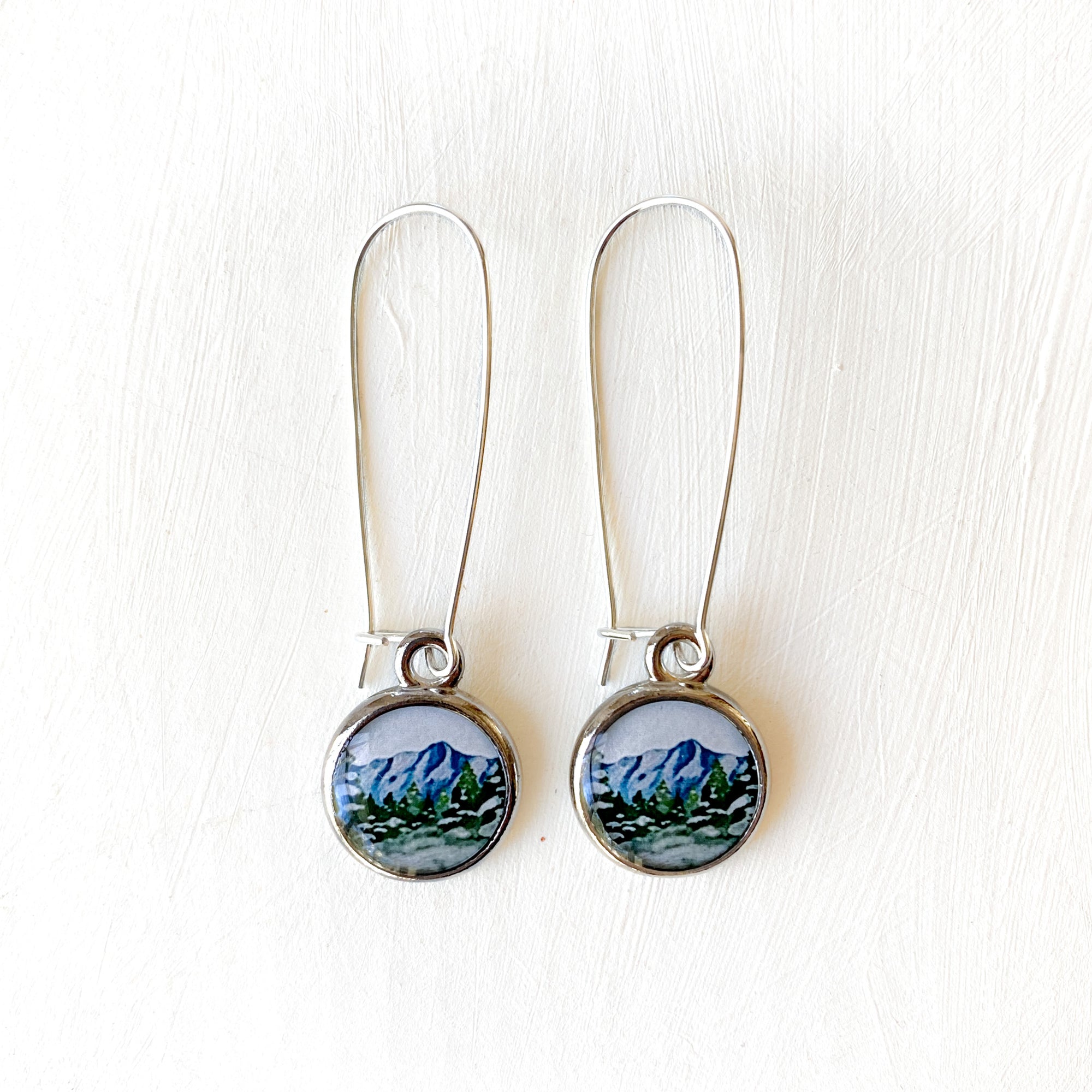 a pair of earrings with a picture of a mountain
