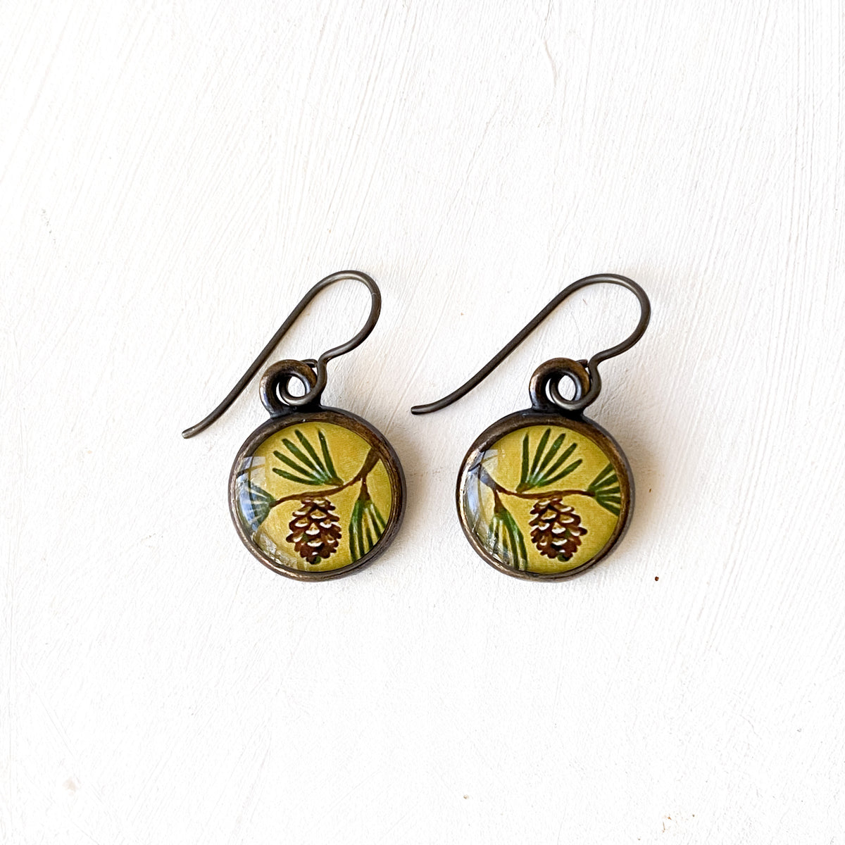 a pair of earrings with a picture of a pine on it