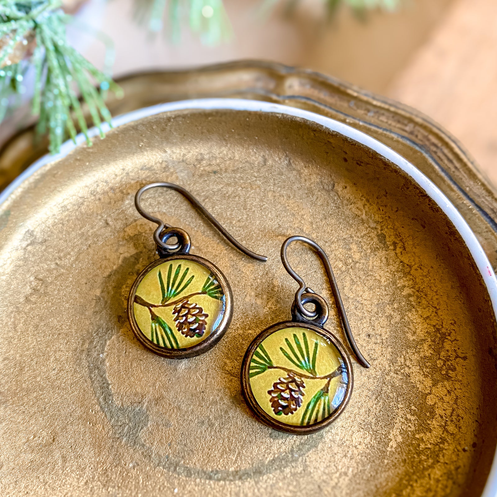 a pair of earrings with a picture of a pine on it
