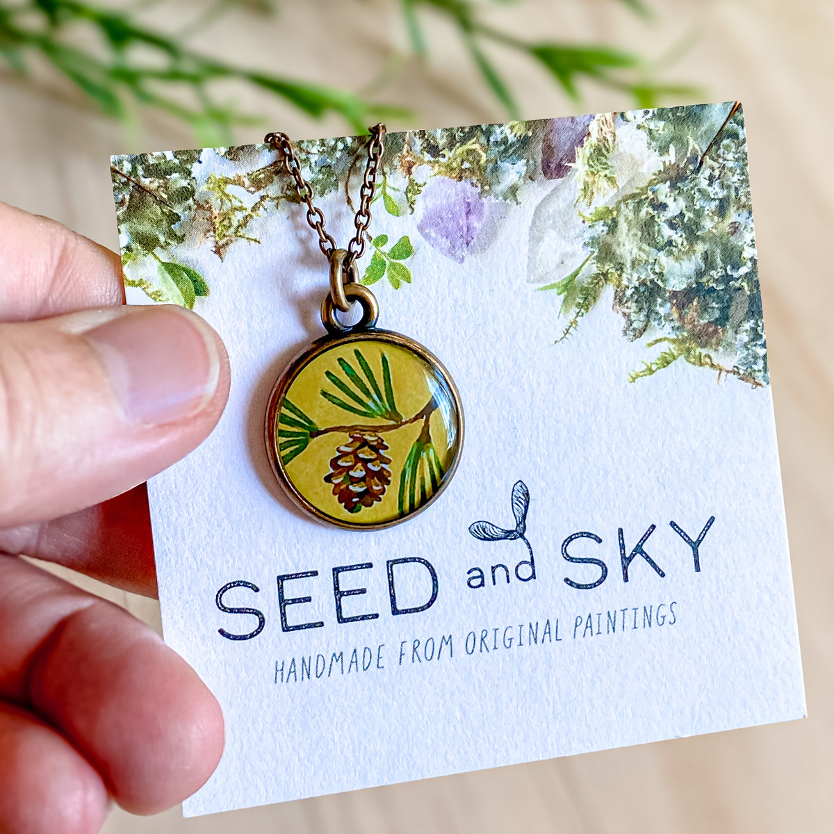 a hand holding a seed and sky pendant